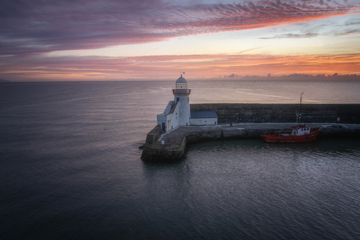 Aerial view of Balbriggan Lighthouse at the end of a stone pier with a red boat docked under a vibrant sunset sky Balbriggan County Dublin Ireland. Aerial view of Balbriggan Lighthouse at the end of a stone pier with a red boat docked under a vibrant sunset sky Balbriggan County Dublin Ireland.