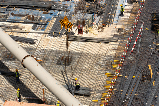 Aerial view of a busy construction site with workers in safety gear laying steel rebar near a large crane hook and industrial piping in Dubai Dubai United Arab Emirates. Aerial view of a busy construction site with workers in safety gear laying steel rebar near a large crane hook and industrial piping in Dubai Dubai United Arab Emirates.