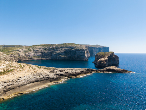 Aerial view of the rugged limestone cliffs and deep blue waters of Dwejra Bay under a clear sky in Gozo Region Malta. Aerial view of the rugged limestone cliffs and deep blue waters of Dwejra Bay under a clear sky in Gozo Region Malta.