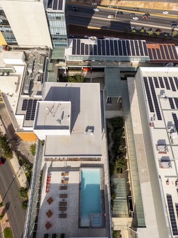 Aerial view of a modern building complex featuring rooftop solar panels a swimming pool with lounge chairs and an adjacent highway in Chihuahua Chihuahua Mexico. Aerial view of a modern building complex featuring rooftop solar panels a swimming pool with lounge chairs and an adjacent highway in Chihuahua Chihuahua Mexico.