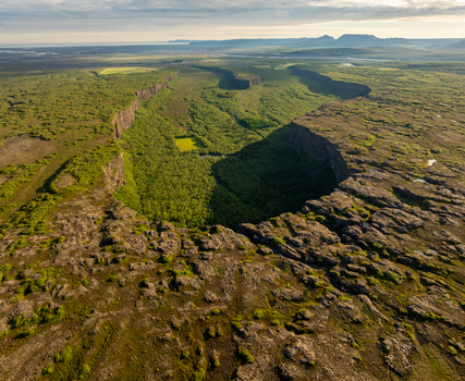 Aerial view of Asbyrgi canyon with its horseshoe shaped cliff walls and lush green forest surrounded by rocky terrain in Nordurthing Iceland.