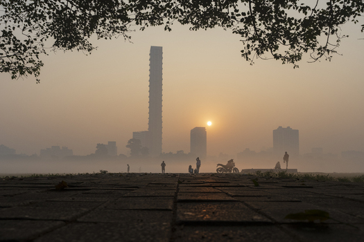 View of a hazy sunrise casting a warm glow over the silhouetted cityscape and the people enjoying the peaceful morning Kolkata West Bengal India. View of a hazy sunrise casting a warm glow over the silhouetted cityscape and the people enjoying the peaceful morning Kolkata West Bengal India.