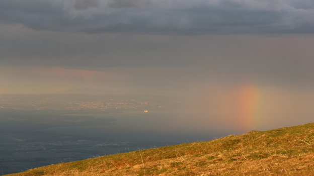 Aerial view of Le Colomby de Gex overlooking the valley Lake Geneva and a distant city under stormy clouds with a rainbow Echenevex Auvergne Rhone Alpes France. Aerial view of Le Colomby de Gex overlooking the valley Lake Geneva and a distant city under stormy clouds with a rainbow Echenevex Auvergne Rhone Alpes France.