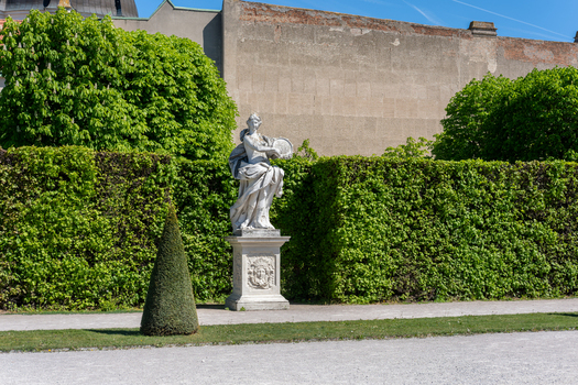 View of a classical marble statue standing in the formal gardens of Belvedere Palace with manicured hedges and lush green trees Vienna Austria. View of a classical marble statue standing in the formal gardens of Belvedere Palace with manicured hedges and lush green trees Vienna Austria.