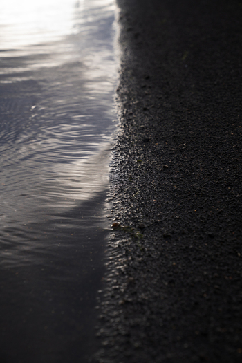 View of glimmering water meets the dark coarse sand under the bright sun creating a stark contrast of light and shadow Skaftárhreppur Skaftárhreppur Iceland. View of glimmering water meets the dark coarse sand under the bright sun creating a stark contrast of light and shadow Skaftárhreppur Skaftárhreppur Iceland.