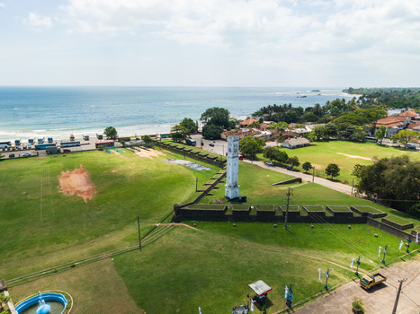 Aerial view of the historic Matara Fort clock tower and stone ramparts overlooking the blue ocean and coastline in Matara Southern Province Sri Lanka. Aerial view of the historic Matara Fort clock tower and stone ramparts overlooking the blue ocean and coastline in Matara Southern Province Sri Lanka.