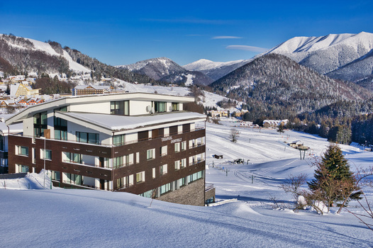 View of a modern brown building stands prominently amidst a snow covered landscape contrasting with the distant mountains under a clear blue sky Donovaly Banska Bystrica Region Slovakia. View of a modern brown building stands prominently amidst a snow covered landscape contrasting with the distant mountains under a clear blue sky Donovaly Banska Bystrica Region Slovakia.