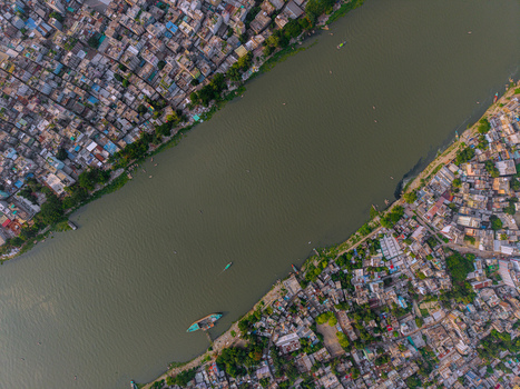 Aerial view of the Buriganga River flowing through dense urban settlements with colorful rooftops and small boats in Keraniganj Dhaka Division Bangladesh. Aerial view of the Buriganga River flowing through dense urban settlements with colorful rooftops and small boats in Keraniganj Dhaka Division Bangladesh.