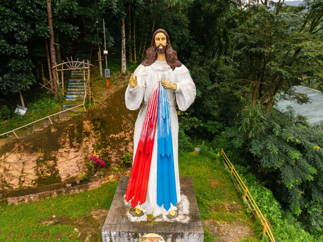 Aerial view of the Divine Mercy statue standing on a hillside surrounded by lush tropical forest and stone stairs in Santa Fe Cagayan Valley Philippines.