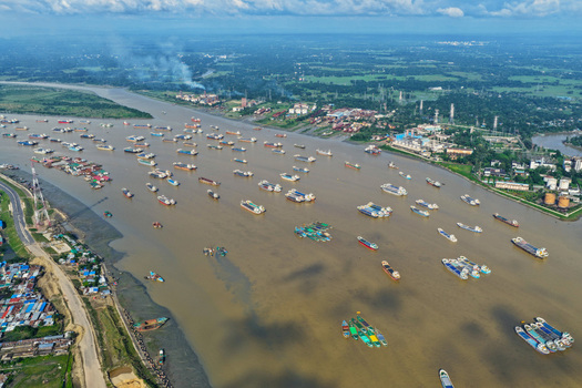 Aerial view of the Karnaphuli River filled with numerous cargo ships and barges anchored near industrial facilities and green banks in Chattogram Chittagong Division Bangladesh.