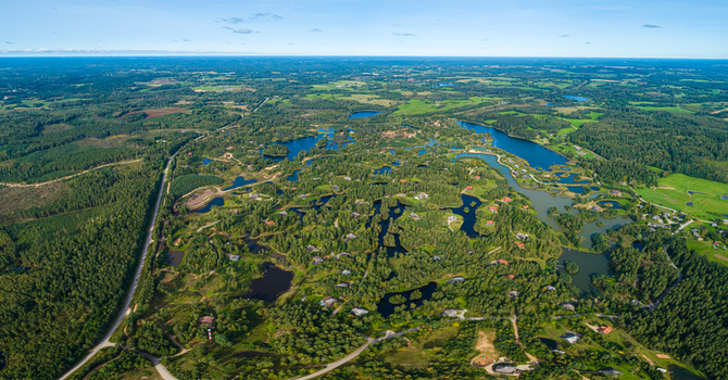 Aerial view of a lush green landscape featuring numerous small lakes dense forests and scattered houses under a clear blue sky Latvia. Aerial view of a lush green landscape featuring numerous small lakes dense forests and scattered houses under a clear blue sky Latvia.