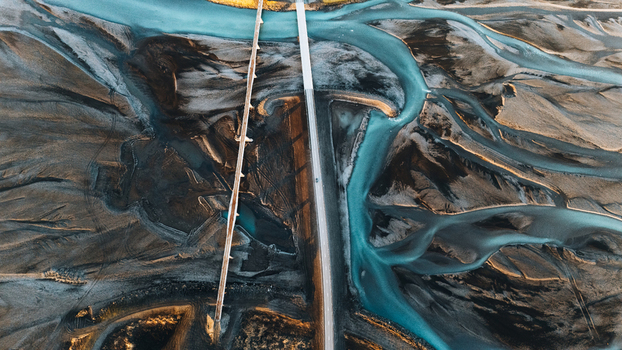 Aerial view of the intricate glacial river braids and a modern bridge crossing the dark volcanic landscape in Skaftarhreppur Iceland.
