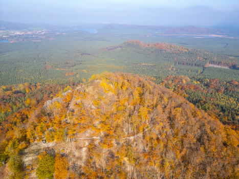 Aerial view of Maly Bezdez hill covered in vibrant autumn foliage surrounded by dense forest and rolling hills in Bezdez Liberecky kraj Czechia.