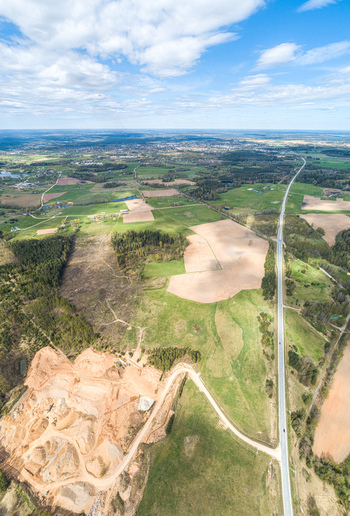 Aerial view of a sand quarry a long road cutting through green fields patches of forest and a distant town under a blue sky in Latvia. Aerial view of a sand quarry a long road cutting through green fields patches of forest and a distant town under a blue sky in Latvia.