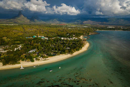 Aerial view of a pristine sandy beach and turquoise lagoon bordered by lush tropical vegetation and dramatic mountain peaks under a cloudy sky Moka District Mauritius. Aerial view of a pristine sandy beach and turquoise lagoon bordered by lush tropical vegetation and dramatic mountain peaks under a cloudy sky Moka District Mauritius.