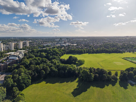 Aerial view of Gunnersbury Park featuring expansive green lawns dense woodland and urban skyline in the background under a bright blue sky in London England United Kingdom. Aerial view of Gunnersbury Park featuring expansive green lawns dense woodland and urban skyline in the background under a bright blue sky in London England United Kingdom.