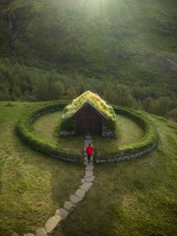 Aerial view of a solitary figure in red approaches a grass roofed church encircled by a vibrant green ring bathed in soft light Selfoss Skeiða og Gnúpverjahreppur Iceland. Aerial view of a solitary figure in red approaches a grass roofed church encircled by a vibrant green ring bathed in soft light Selfoss Skeiða og Gnúpverjahreppur Iceland.