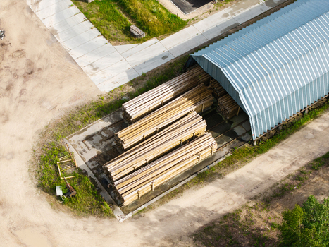 Aerial view of stacked timber logs stored under a metal roof structure in a forestry facility in Latvia. Aerial view of stacked timber logs stored under a metal roof structure in a forestry facility in Latvia.