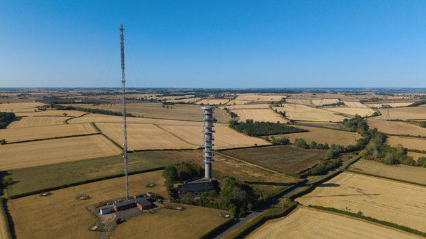 Aerial view of the Morborne Hill Transmitter with its tall lattice mast and concrete tower surrounded by golden agricultural fields in Morborne England United Kingdom. Aerial view of the Morborne Hill Transmitter with its tall lattice mast and concrete tower surrounded by golden agricultural fields in Morborne England United Kingdom.