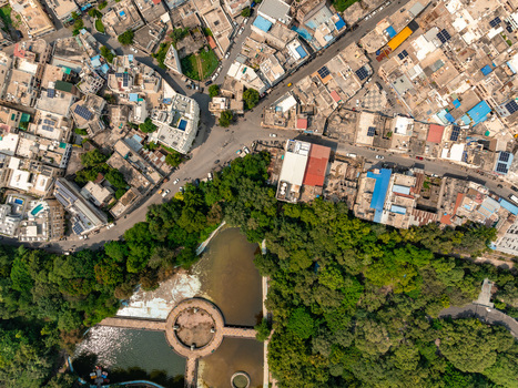 Aerial view of a dense urban intersection featuring a lush green park and a circular water feature surrounded by historic buildings and rooftops in Udaipur Rajasthan India. Aerial view of a dense urban intersection featuring a lush green park and a circular water feature surrounded by historic buildings and rooftops in Udaipur Rajasthan India.