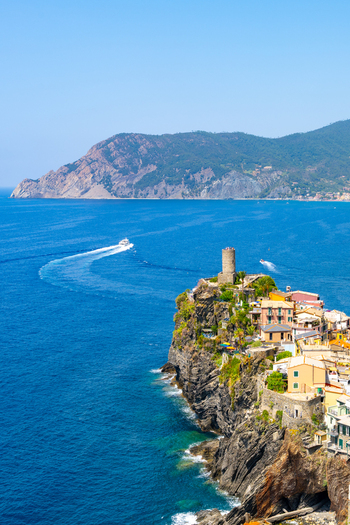 View of the historic village of Vernazza in Cinque Terre perched on cliffs above the Mediterranean Sea with colorful buildings a stone tower and a boat in Vernazza Liguria Italy.