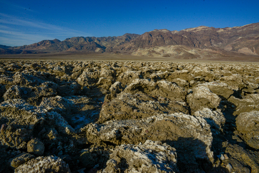 View of the rugged salt formations at the Devil s Golf Course in Death Valley National Park with distant mountains under a clear blue sky in Death Valley California United States.