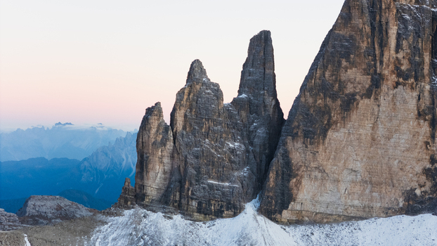 Aerial view of Tre Cime di Lavaredo peaks with snow covered slopes and distant mountain ranges under a soft twilight sky Auronzo di Cadore Veneto Italy. Aerial view of Tre Cime di Lavaredo peaks with snow covered slopes and distant mountain ranges under a soft twilight sky Auronzo di Cadore Veneto Italy.