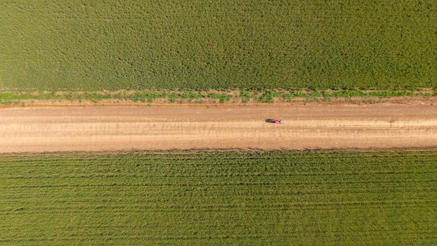 Aerial view of a dirt road cutting through vibrant green agricultural fields with a small vehicle driving along the path in Greyton Western Cape South Africa.