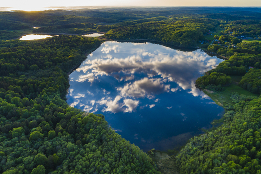 Aerial view of Sandsjobacka Naturreservat with a calm lake reflecting the sky and clouds surrounded by lush green forests during golden hour in Molndal Vastra Gotaland County Sweden.