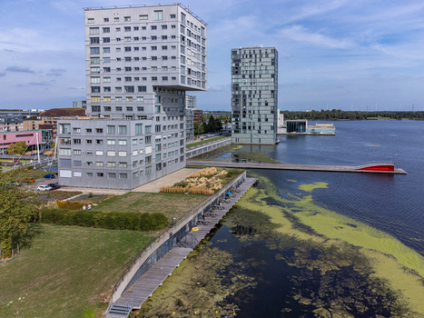 Aerial view of modern architecture reflected in the water with a walkway and green spaces creating a vibrant contrast against the sky Silverline Flevoland Netherlands. Aerial view of modern architecture reflected in the water with a walkway and green spaces creating a vibrant contrast against the sky Silverline Flevoland Netherlands.