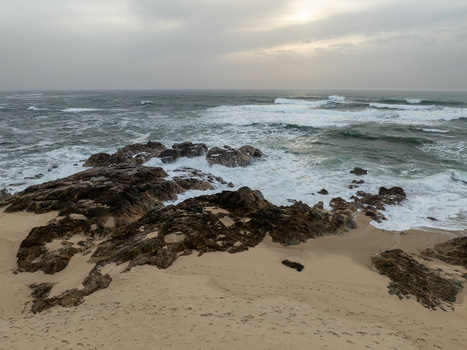 Aerial view of the turbulent ocean crashing against the rugged dark rocks and sandy beach under a grey overcast sky Vila Chã Portugal. Aerial view of the turbulent ocean crashing against the rugged dark rocks and sandy beach under a grey overcast sky Vila Chã Portugal.