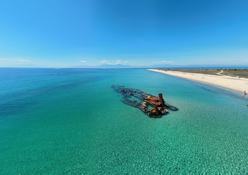 Aerial view of the rusty Shipwreck Epanomi submerged in turquoise waters along a sandy beach under a clear blue sky in Epanomi Greece.