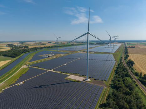Aerial view of a large solar farm with wind turbines set amidst agricultural fields and canals in the Netherlands.