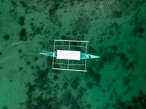 Aerial view of a traditional outrigger boat gliding through the clear turquoise waters of Sugba Lagoon in Del Carmen Caraga Philippines. Aerial view of a traditional outrigger boat gliding through the clear turquoise waters of Sugba Lagoon in Del Carmen Caraga Philippines.