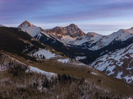 Aerial view of Capitol Peak illuminated by the warm glow of a winter sunset featuring snow capped mountain ridges and dense evergreen forests. Aspen Colorado United States.