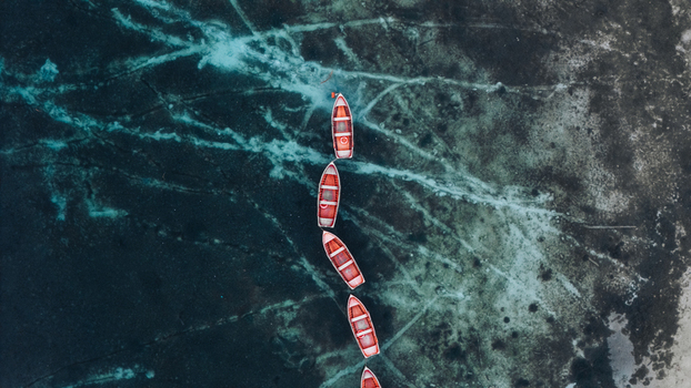 Aerial view of red wooden rowing boats floating on the clear turquoise waters of Lake Braies showing the rocky lakebed from above in Braies Trentino Alto Adige Italy. Aerial view of red wooden rowing boats floating on the clear turquoise waters of Lake Braies showing the rocky lakebed from above in Braies Trentino Alto Adige Italy.