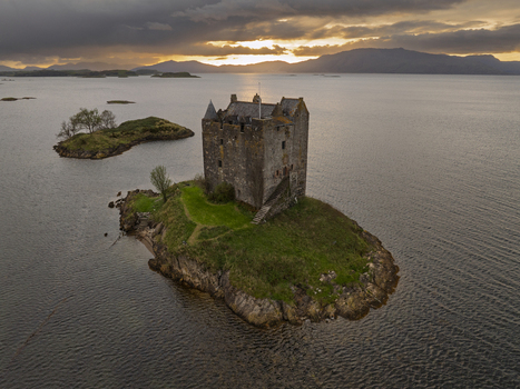 Aerial view of the historic Castle Stalker situated on a small island in a loch surrounded by calm water and distant mountains under a dramatic golden hour sky Scotland United Kingdom. Aerial view of the historic Castle Stalker situated on a small island in a loch surrounded by calm water and distant mountains under a dramatic golden hour sky Scotland United Kingdom.