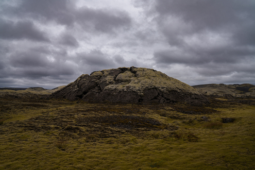 View of a moss covered hill under a cloudy sky standing stark against the textured landscape creating a scene of Icelandic beauty Skaftárhreppur Iceland. View of a moss covered hill under a cloudy sky standing stark against the textured landscape creating a scene of Icelandic beauty Skaftárhreppur Iceland.