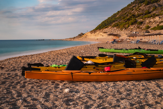 View of yellow and green kayaks resting on the sandy shore where the turquoise sea meets the land under a serene sky Lefkada Greece. View of yellow and green kayaks resting on the sandy shore where the turquoise sea meets the land under a serene sky Lefkada Greece.