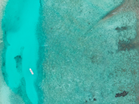Aerial view of a solitary boat glides across the turquoise channel bisecting the textured coral reefs below Vashafaru Island Thiladhummathi Atoll Maldives. Aerial view of a solitary boat glides across the turquoise channel bisecting the textured coral reefs below Vashafaru Island Thiladhummathi Atoll Maldives.