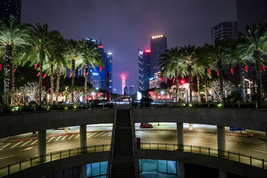 Guangzhou China 24 February 2024 View of the illuminated modern skyline at night featuring towering skyscrapers palm trees with red lanterns and a pedestrian overpass. Guangzhou China 24 February 2024 View of the illuminated modern skyline at night featuring towering skyscrapers palm trees with red lanterns and a pedestrian overpass.