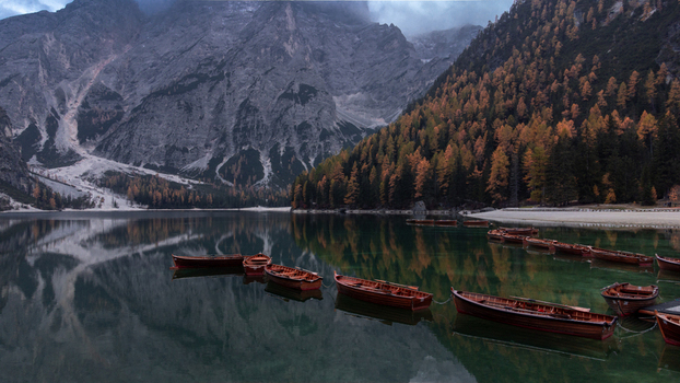 Aerial view of Pragser Wildsee featuring wooden boats moored on the calm lake surface surrounded by autumn foliage and dramatic mountain peaks in Prags Trentino Alto AdigeS Italy.