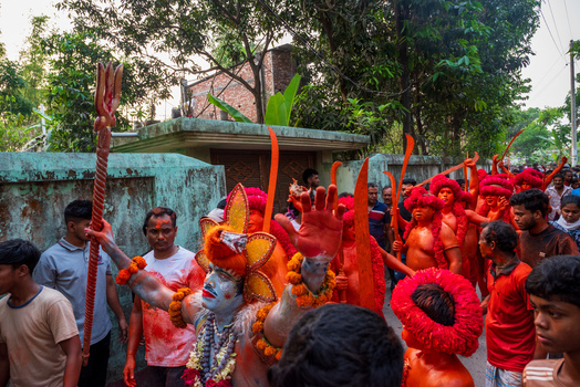 Munshiganj Bangladesh 13 April 2026 View of a religious procession with devotees painted in orange and a central figure dressed as a deity holding a trident.