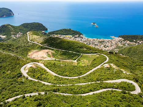 Aerial view of the winding road through lush green hills leading to the coastal town of Petrovac Budva Municipality Montenegro.