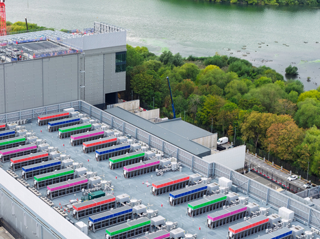 Aerial view of Data Center featuring rows of colorful cooling units on the rooftop situated next to a river and lush green trees in the United Kingdom.