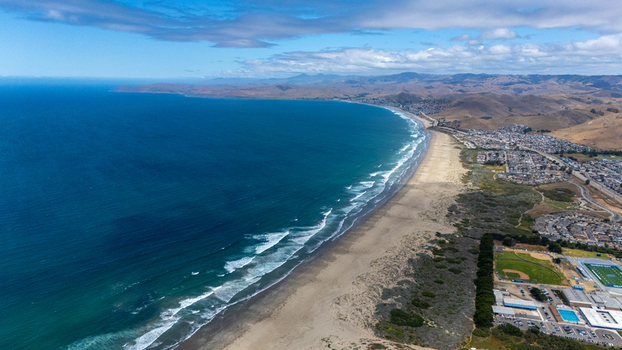 Aerial view of the expansive coastline with a long sandy beach rolling waves and a coastal town nestled against the hills in Morro Bay California United States.