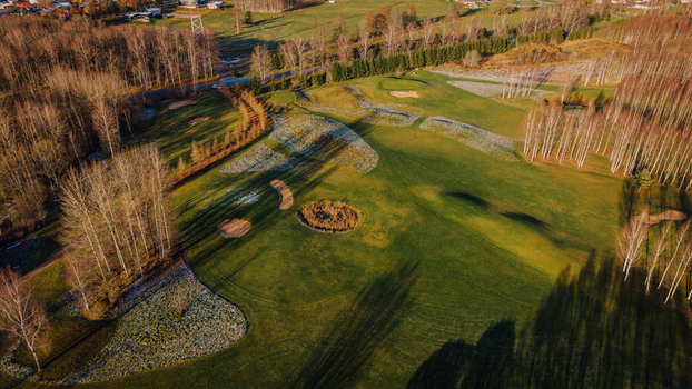 Valmiera Latvia 18 November 2025 Aerial view of a golf course featuring frosty grass sand bunkers and surrounding birch trees under golden morning light.