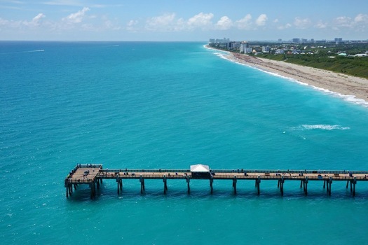 Aerial view of the Juno Beach Pier stretching into turquoise ocean waters along the sandy coastline with people fishing in Juno Beach Florida United States. Aerial view of the Juno Beach Pier stretching into turquoise ocean waters along the sandy coastline with people fishing in Juno Beach Florida United States.