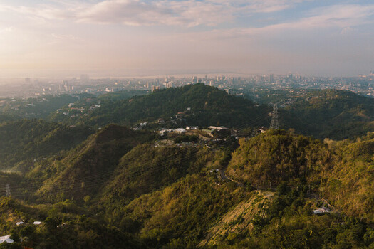 Aerial view of Busay hills overlooking the urban skyline and coastal landscape under a soft sunset sky Cebu City Central Visayas Philippines.