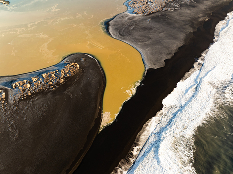 Aerial view of the dramatic contrast between the dark black sand beach and the golden river water meeting the white surf of the Atlantic Ocean in Reykjanesbaer Iceland. Aerial view of the dramatic contrast between the dark black sand beach and the golden river water meeting the white surf of the Atlantic Ocean in Reykjanesbaer Iceland.
